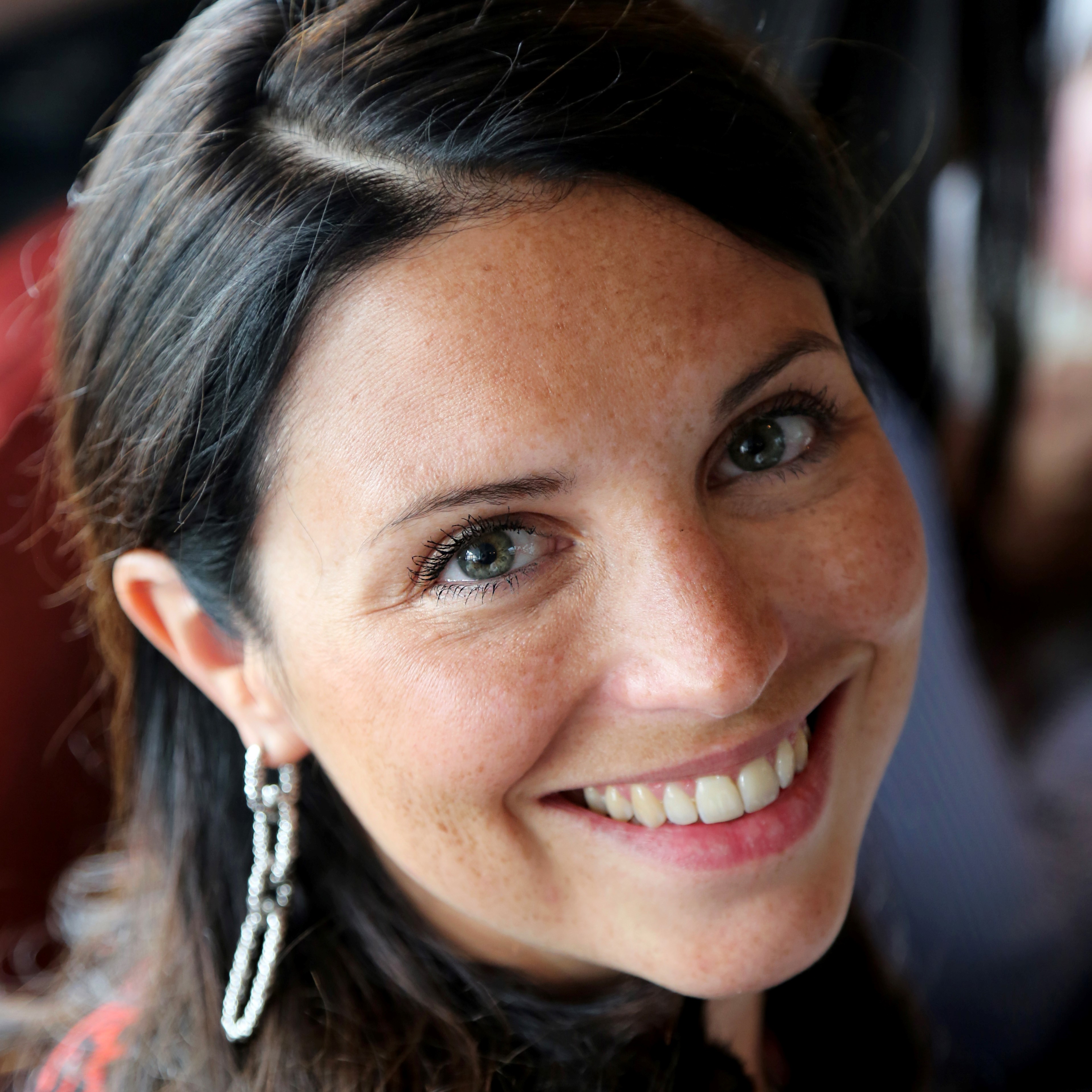 Personne souriant à la caméra avec des boucles d'oreilles étincelantes.