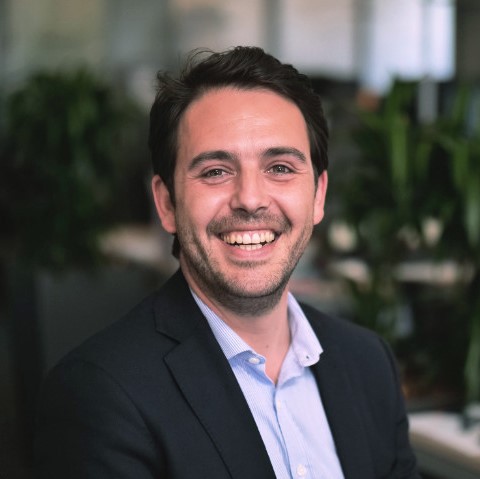 Personne souriante dans un bureau avec des plantes en arrière-plan.