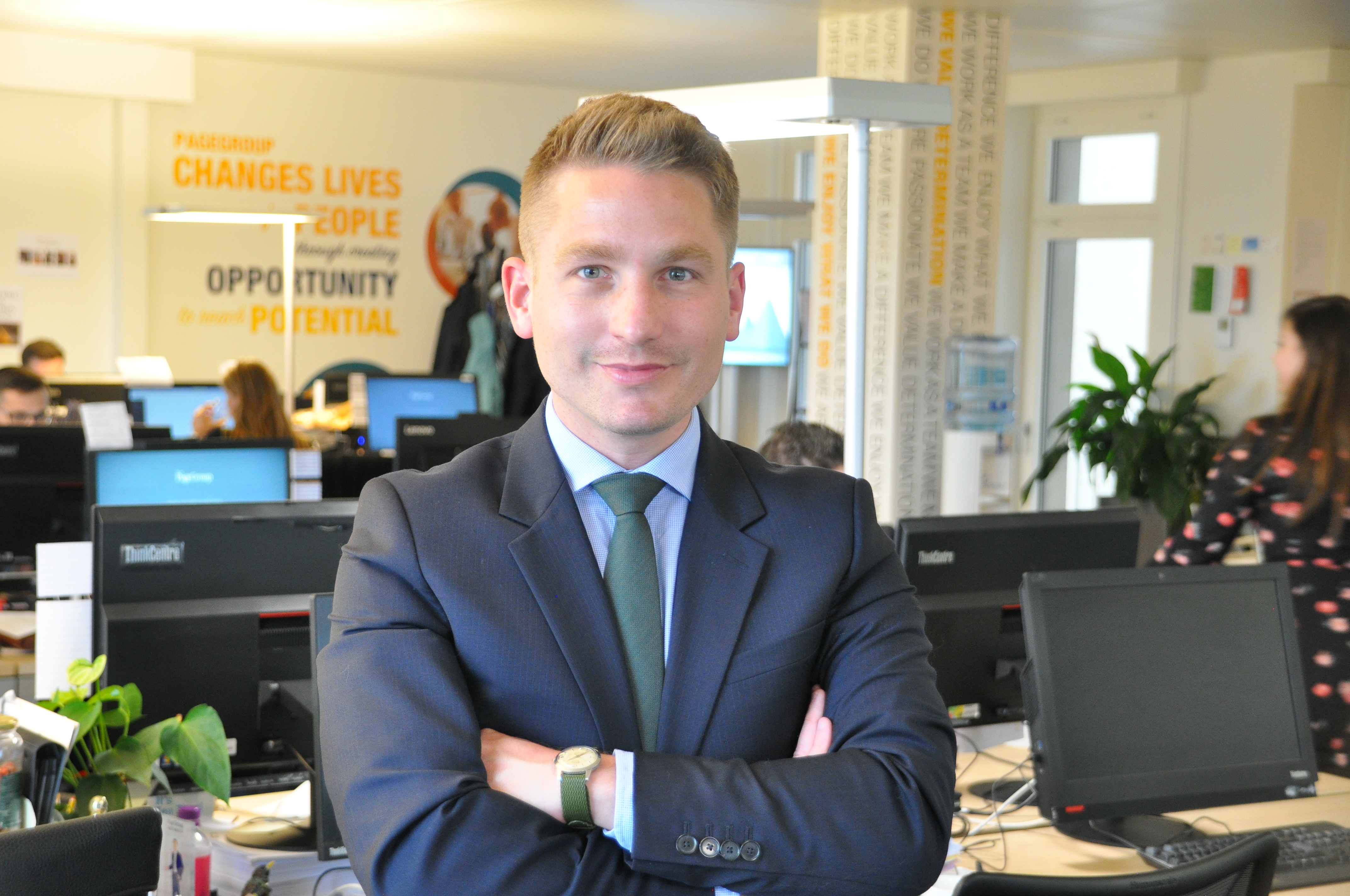 Person in a suit with arms crossed in an office setting.