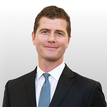 Person in a suit smiling against a plain background