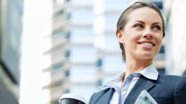 Personne souriant dehors avec une tasse de café et des documents.