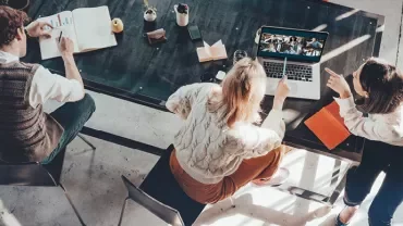 Three people working at a table with a laptop in a casual setting.