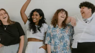 Four friends laughing together in a light-filled room.