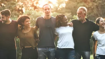 Group of people standing together outdoors, smiling at each other.