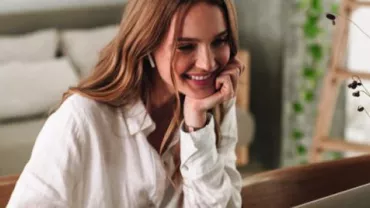 Person smiling while using a laptop at home.