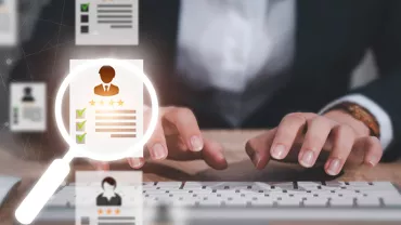 Person typing on keyboard, selecting a resume through magnifying glass.