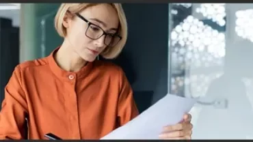 Woman with blonde hair and glasses reading a piece of paper