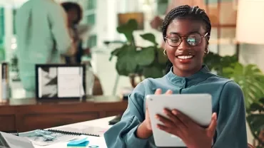 A smiling woman at the office using an iPad