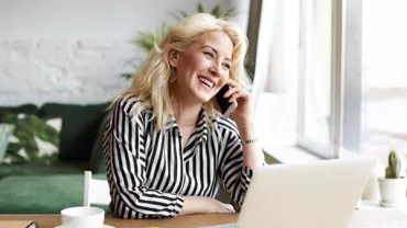 Personne souriant lors d'un appel téléphonique en utilisant un ordinateur portable.