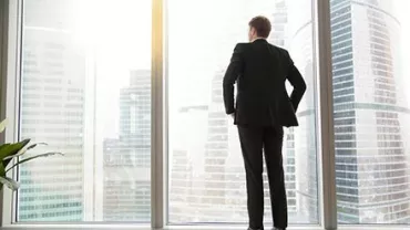 Personne en costume regarde la ville à travers de grandes fenêtres.