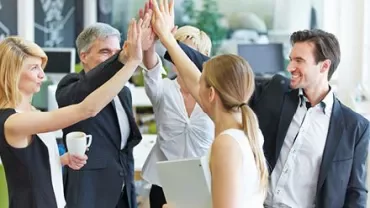 Group of colleagues celebrating with high fives in an office.