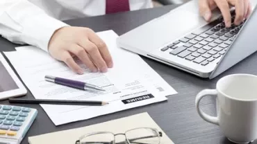 Personne travaillant sur un ordinateur portable avec des documents de CV sur le bureau.