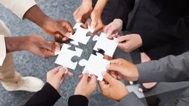 Groupe de mains assemblant des pièces de puzzle sur un fond gris.