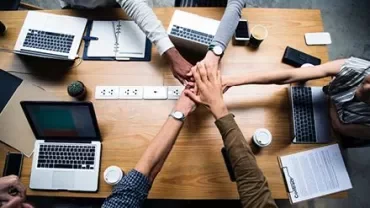 Groupe de personnes joignant les mains au-dessus d'un bureau avec des ordinateurs portables et du café.