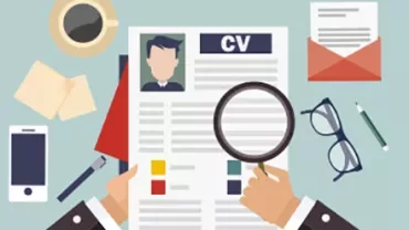 Person reviewing CV with magnifying glass on cluttered desk.