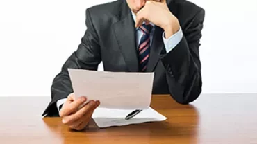 Person in suit reading a document at a desk.