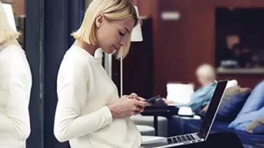 Person sitting by window with laptop and phone.