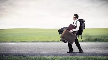 Person walking on road carrying multiple bags.