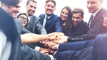 Group of people in business attire joining hands in teamwork.
