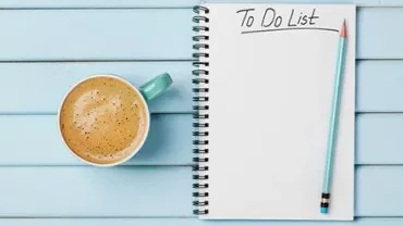 Spiraalnotitieboek met 'To Do List,' blauw potlood, en een kop koffie op een houten tafel.