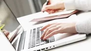 Persoon typt op een laptop aan een bureau.