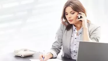 Persoon aan de telefoon schrijft aan een bureau met een laptop.