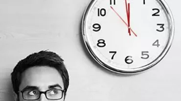 Personne avec des lunettes regardant une horloge murale.
