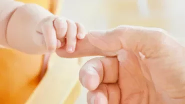 Een baby houdt de vinger van een volwassene vast.