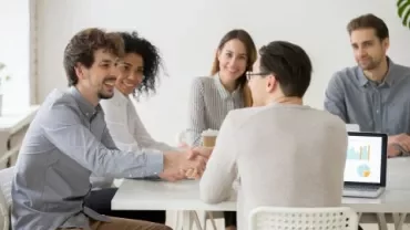 People sitting at a table having a meeting, one person shaking hands.