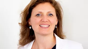 Person smiling, wearing a white jacket and earrings.