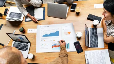 Mensen bespreken grafieken en data aan een vergadertafel met laptops.