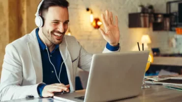 Personne souriante saluant lors d'un appel vidéo sur un ordinateur portable.