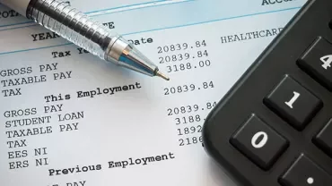 Close-up of a payslip with a pen and calculator on a table.