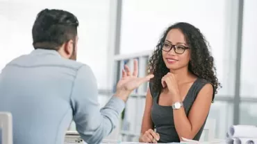 Twee mensen in gesprek aan een tafel in een kantooromgeving.