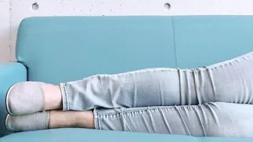 Personne allongée sur un canapé turquoise, jambes étendues en jean clair et chaussons.