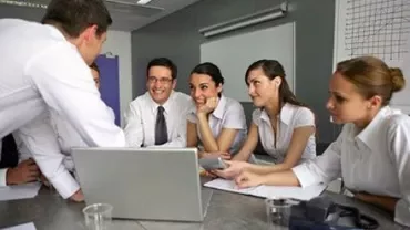 Mensen in een vergadering rond een laptop, lachend en pratend.