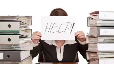 Personne tenant une pancarte 'HELP!' derrière des piles de dossiers.