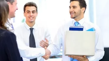 Office workers shaking hands, one holding a box.