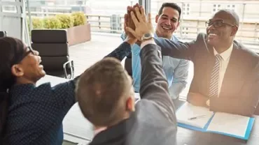 Business team celebrating with a high five at a meeting.