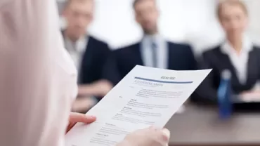 Person holding a resume in front of a panel during a job interview.