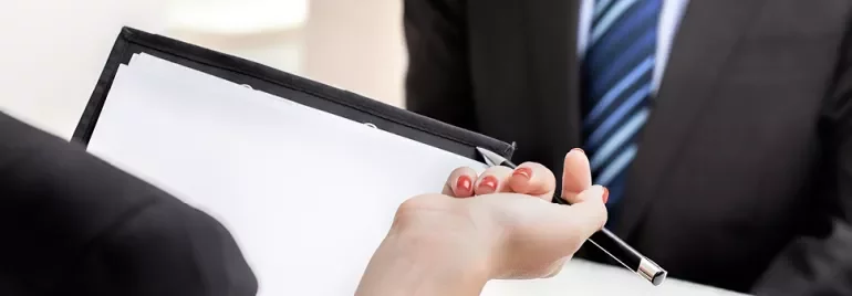 Hands holding a clipboard with a blank paper and a pen.