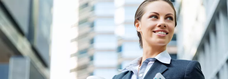 Person in business attire holding coffee and tablet outdoors.