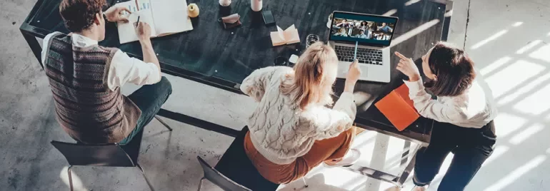 Drie mensen werken aan een tafel met een laptop.
