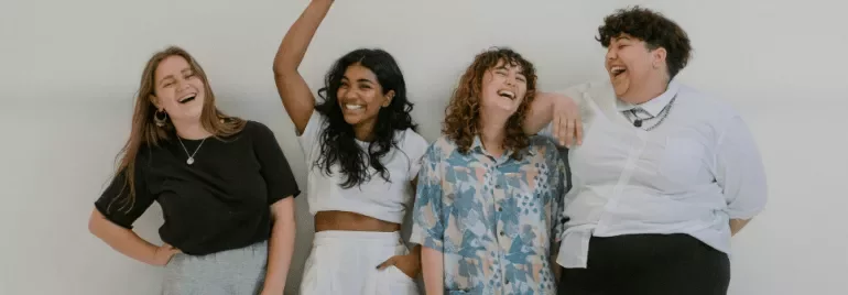 Vier vrienden lachen samen in een lichte kamer.