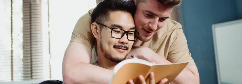 Two people smiling and reading a notebook together.