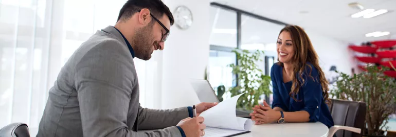 Deux personnes à une table dans un bureau, discutant et regardant des documents.