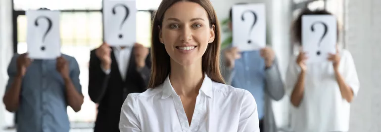 Person smiling in front of others holding question mark signs over faces.