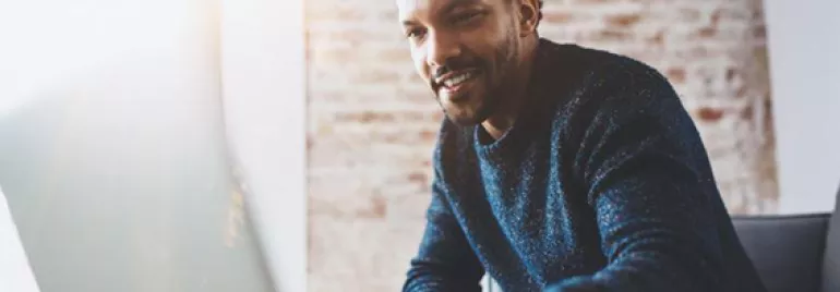 Personne souriant devant un ordinateur portable dans une pièce ensoleillée.