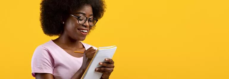 Personne écrivant dans un carnet, souriant sur un fond jaune.