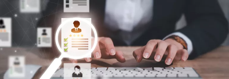 Personne tapant sur un clavier, sélectionnant un CV à travers une loupe.